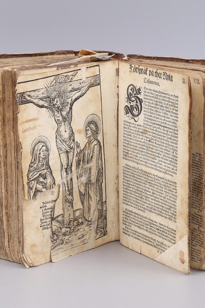 Bild på uppslagen gammal bok. Bilden till vänster har en bild av Jesus på korset.